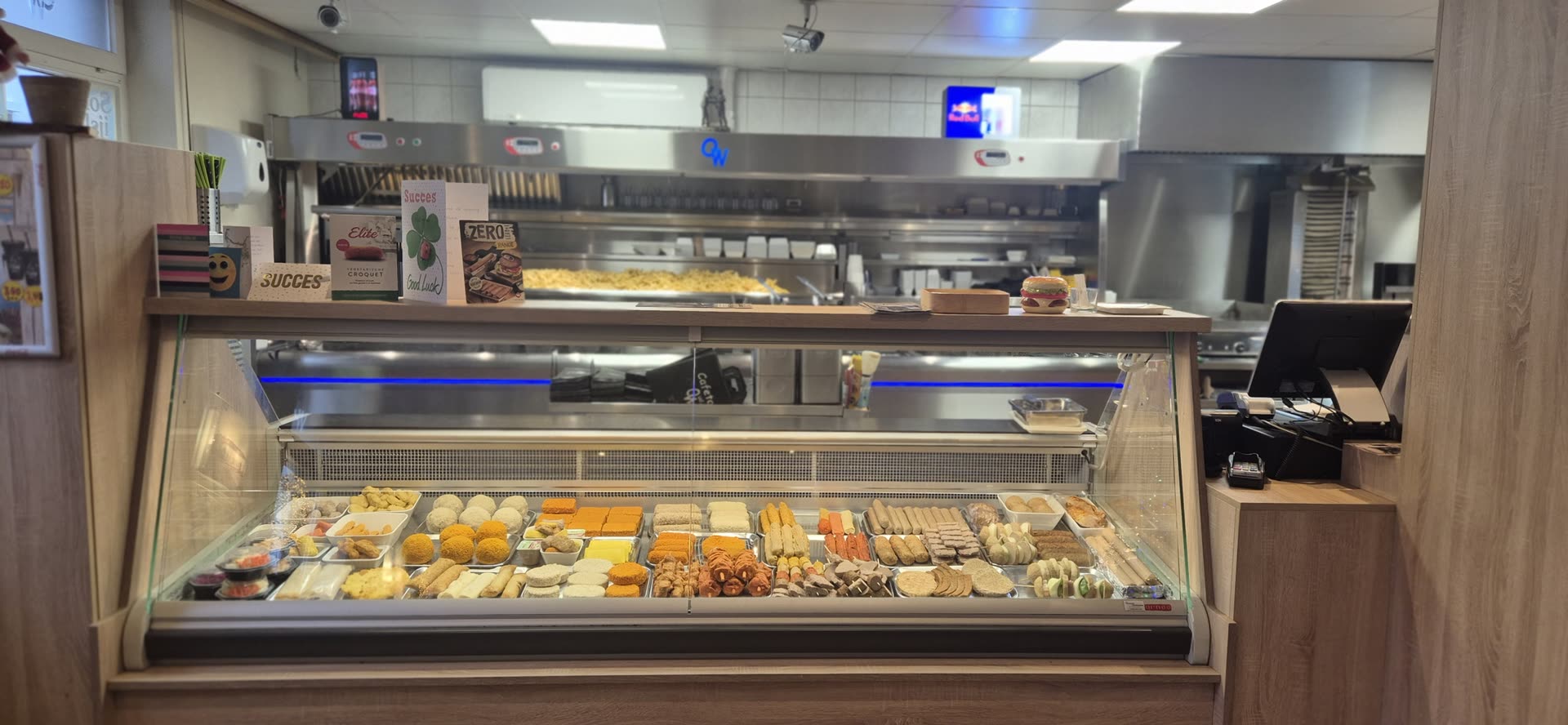 De toonbank van Cafetaria Oud Waubach met de snackvitrine; op de afzuigkap erachter staat het OW-beeldmerk van de zaak.